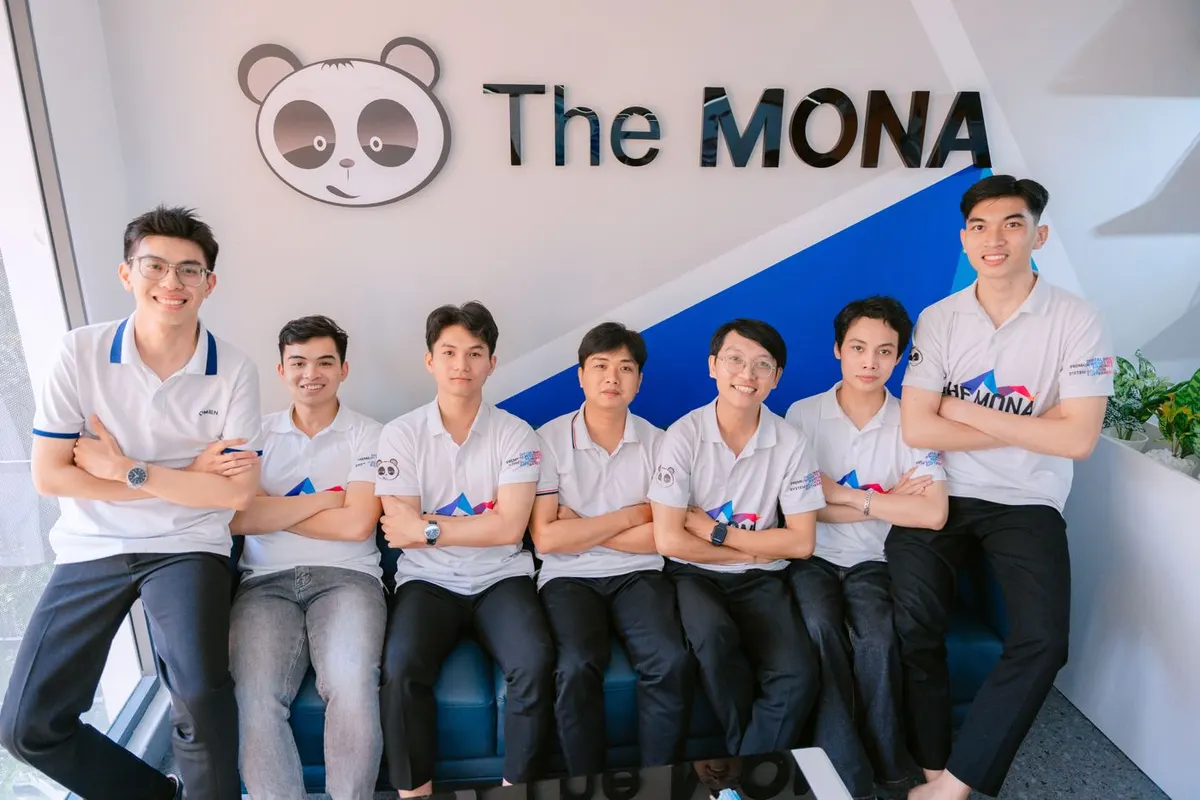 Đội ngũ MONA đứng trước bảng logo công ty